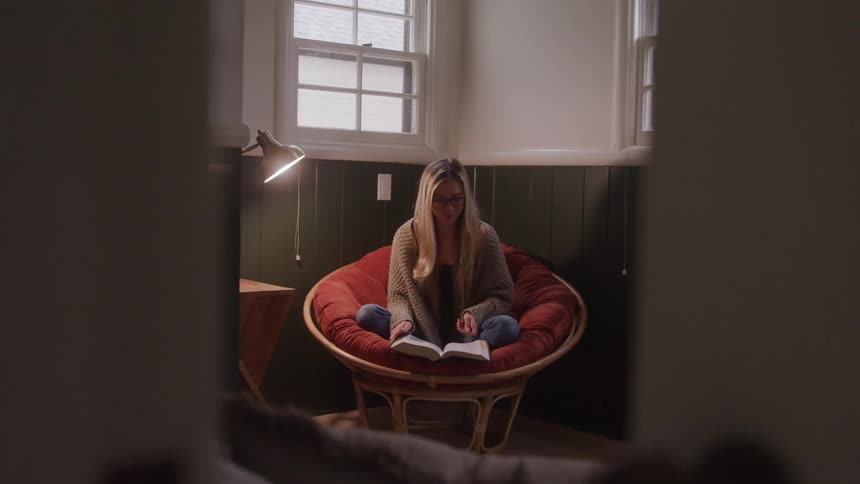 A woman engrossed in a book bathed in soft light within a cozy woodpaneled room
