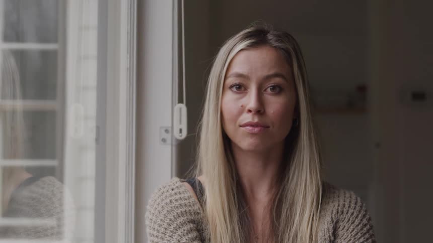 A woman near a window looking straight ahead with a focused and intense gaze