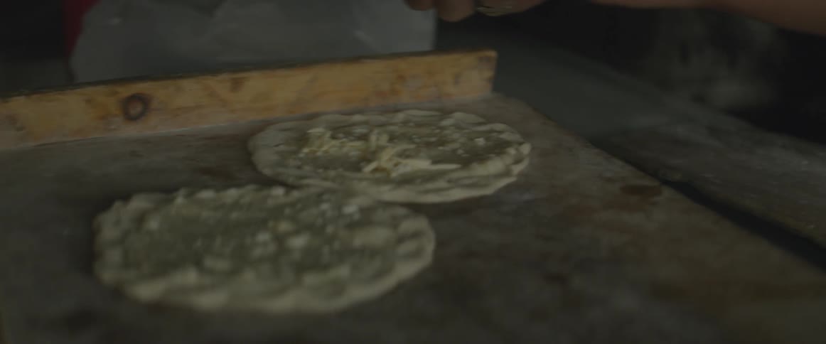A person is putting cheese on some dough