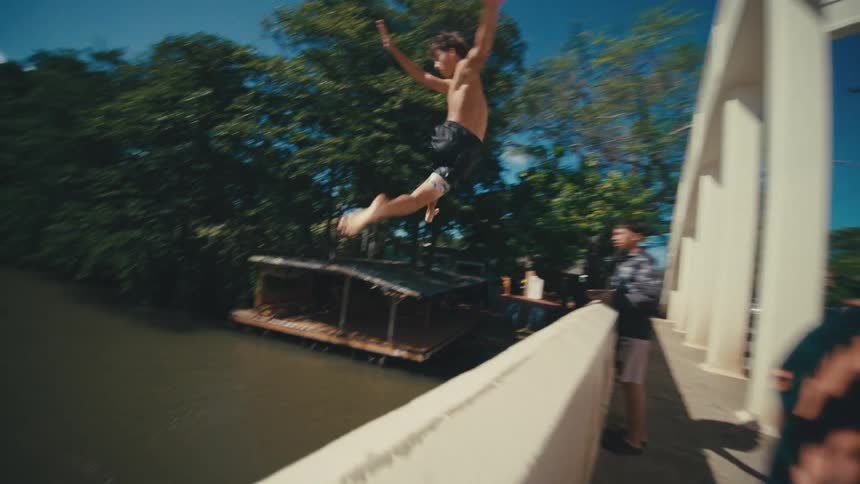 The teenager jumps off the bridge and splashes in the water