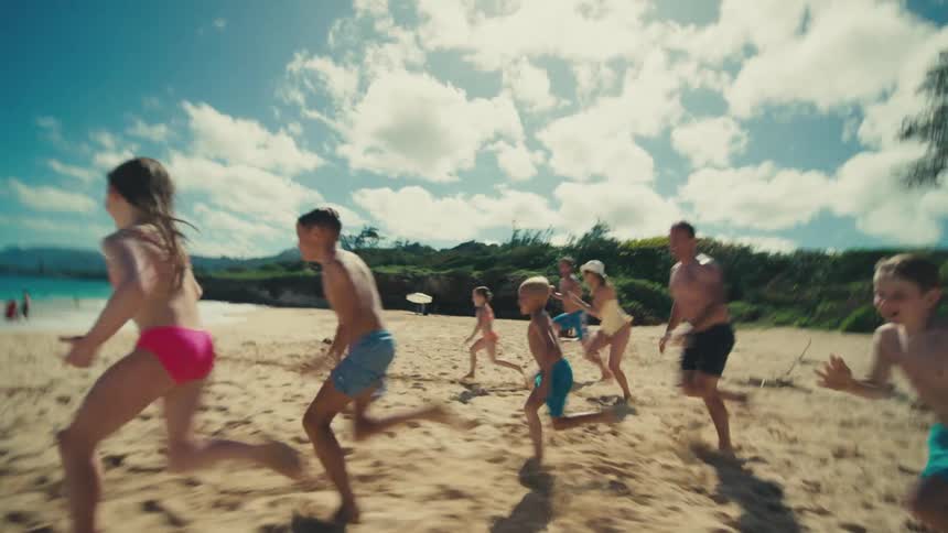 Group of people including adults and children running quickly towards the sea on the beach