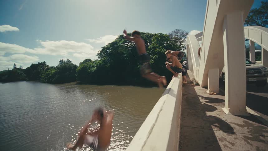 Group of boys jumping off a bridge into a river