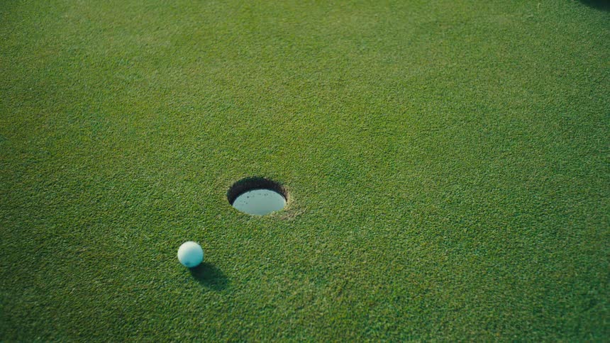 White ball approaches the hole on a neatly trimmed golf course green