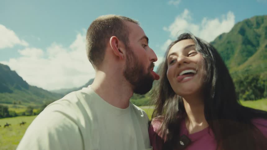 Couple smiles surrounded by mountainous nature under a sunny blue sky