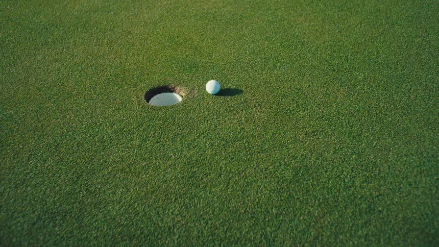 A golf ball stops just short of the hole as a persons foot steps into frame