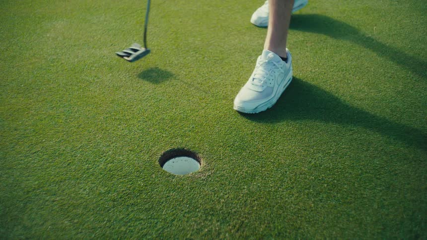 A man scores in golf and pulls the ball out of the hole
