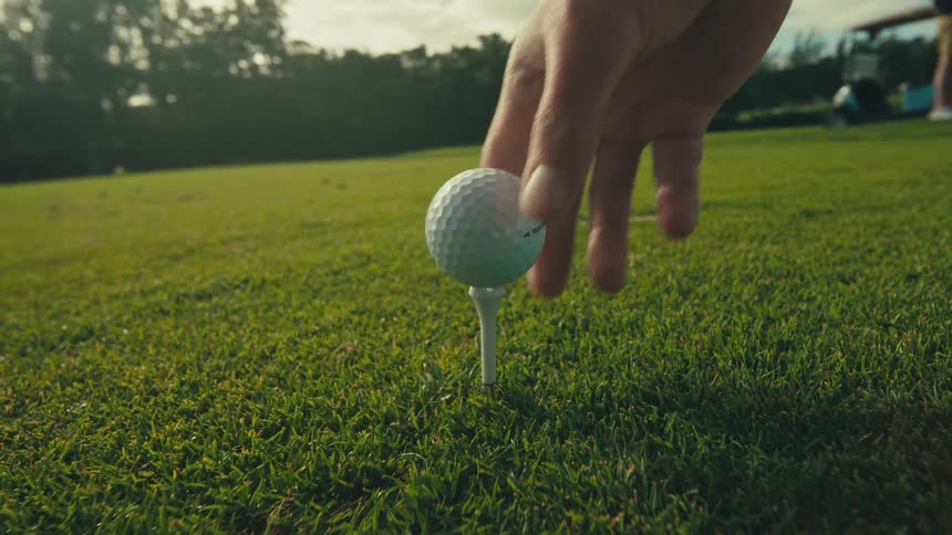 Hand placing a golf ball into a holder on a lawn