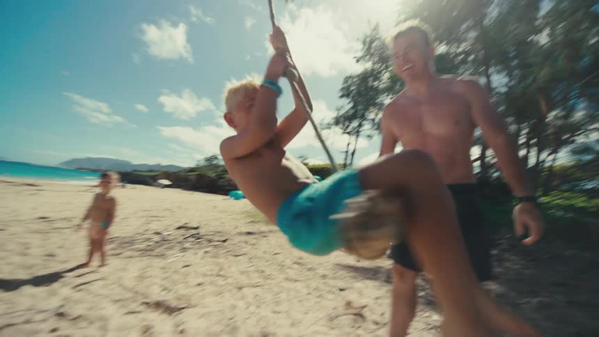 Boy on the beach being pushed on a swing by his father
