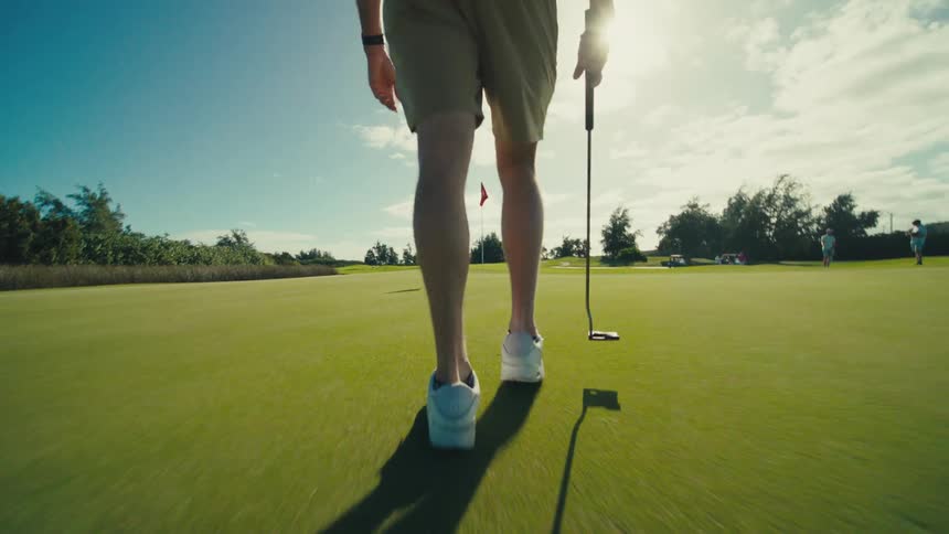 Man carrying a putter walks toward the hole on the golf course