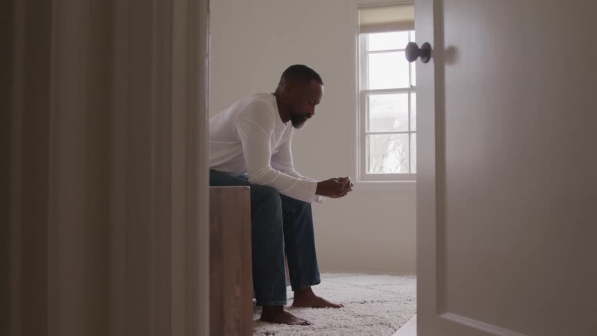 Man sitting on the edge of the bed looks at something in his hands