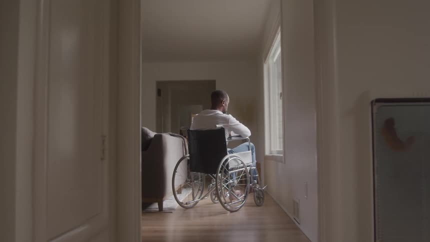 The man sits in a wheelchair by the window