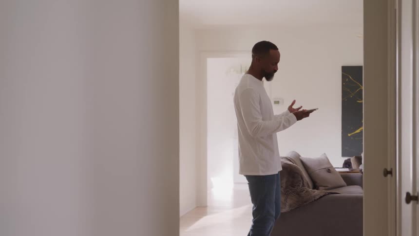 A man walks back and forth in his living room talking to someone on the other end of the smartphone in his hand