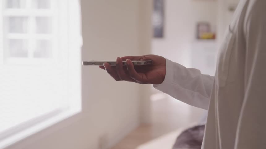 A black person stands gesturing with a hand while holding a phone in a well lit room