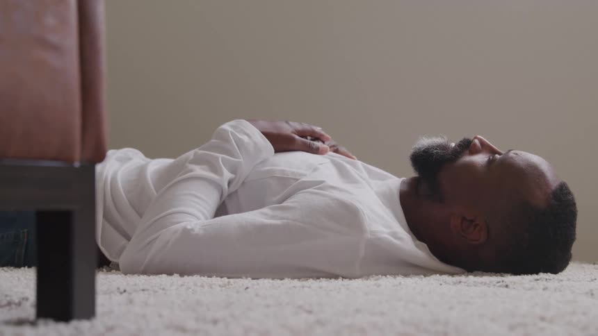 A black man is laying on a white rug on the floor thinking as he looks ahead