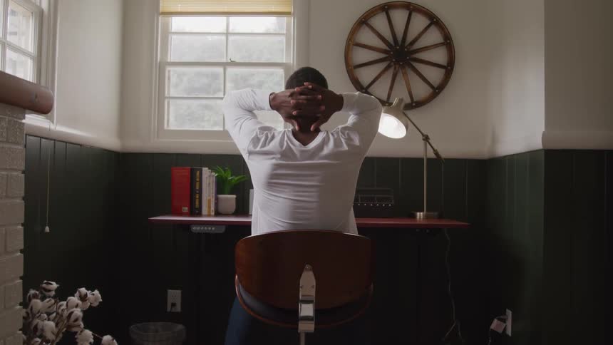 Man sitting at a desk puts his hands behind his head