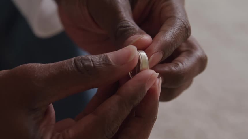 A closeup shot shows darkskinned hands delicately holding and examining a silver ring against a blurred light background