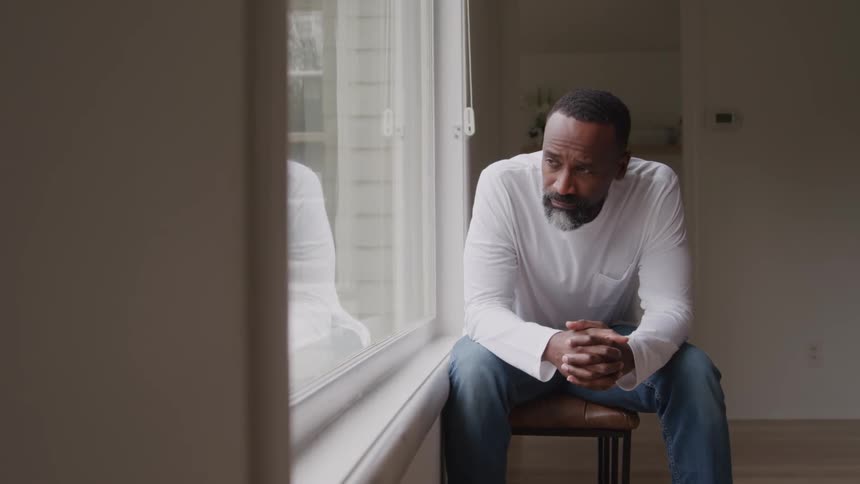 Man sitting and thoughtfully looking out the window with hands clasped