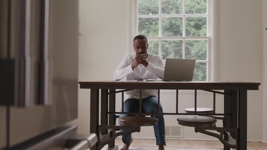 Homem sentado mesa cobre o rosto com as mos diante de um notebook em ambiente iluminado