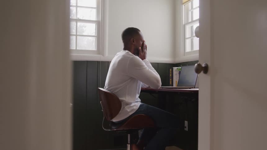 Man working in front of a laptop and putting his hands to his face