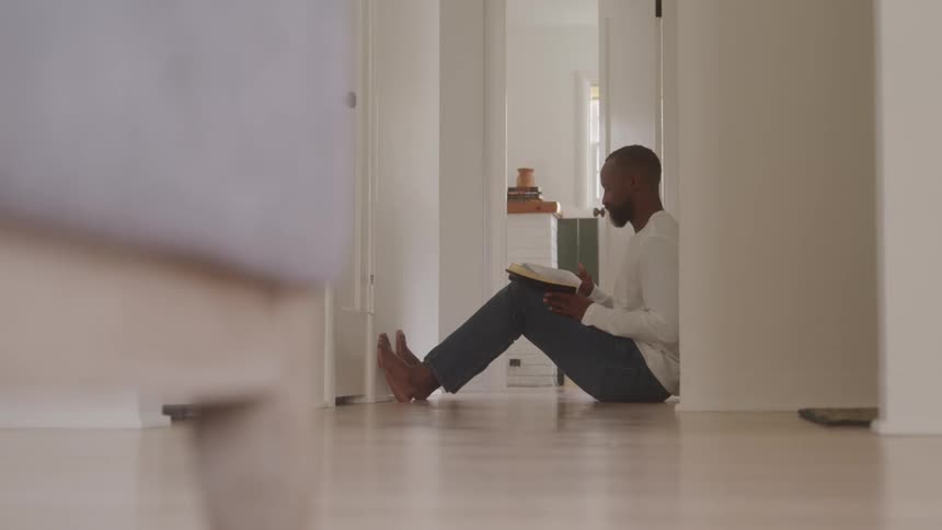 Man sitting in the hallway reads a book with his back against the wall