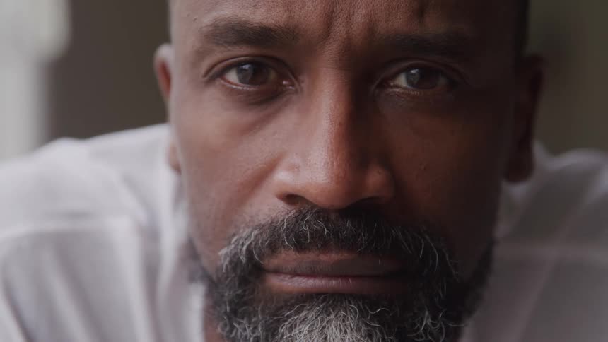 A closeup of a mans face reveals deep reflective eyes and a calm but serious sad expression