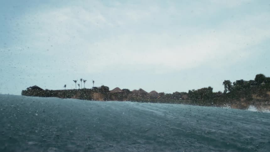 View from inside the sea of an ocean wave passing by and the coast in the background