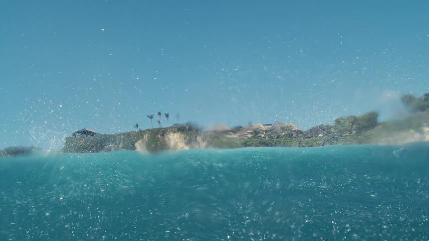 View from inside the sea of a crystalline wave passing with the coast in the background