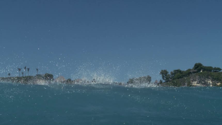 Crystal clear ocean wave breaking with the coast in the background