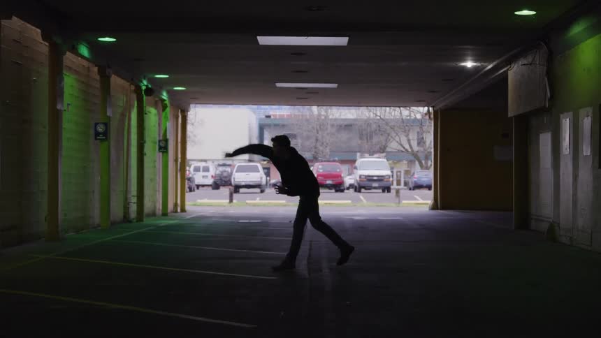 Silhouette of a man throwing his cell phone at the wall of a parking lot