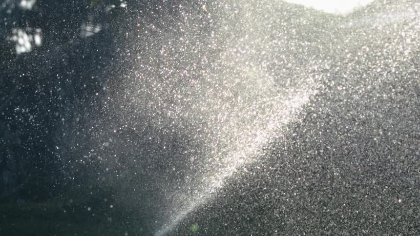 Sprinkler sprays fine jets of water illuminated by sunlight