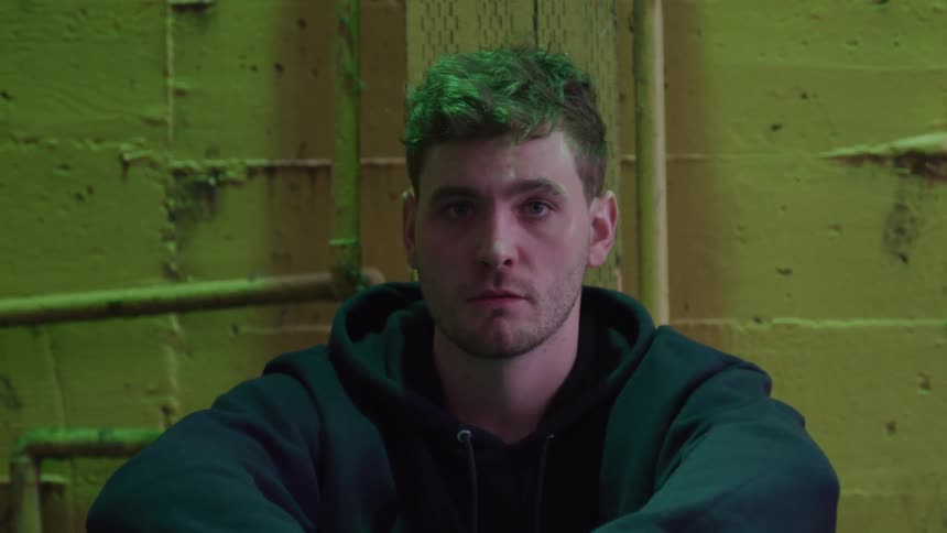 The man is sitting up against the yellow wall