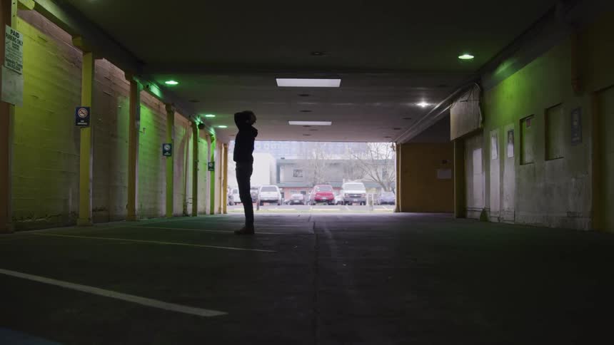 Person crouching holds their head with both hands inside a covered parking garage