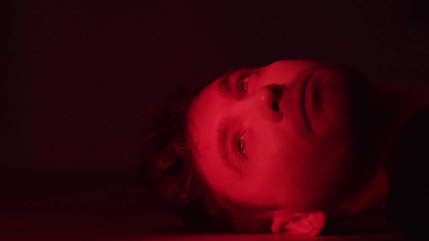 Mans face lit by intense red light rests on the floor