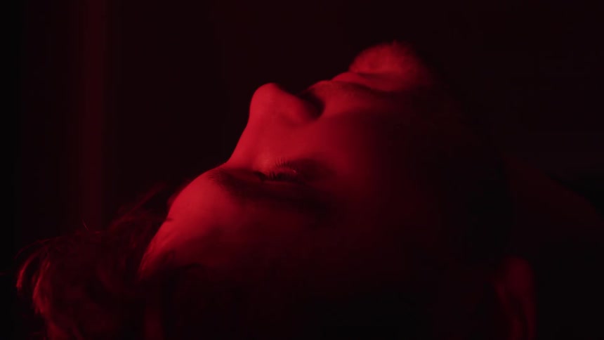 Male face seen in profile is lit by intense red light while lying down