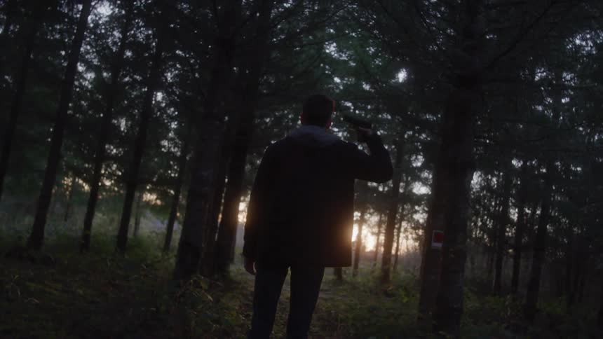 Man putting a gun to his head while standing in a forest
