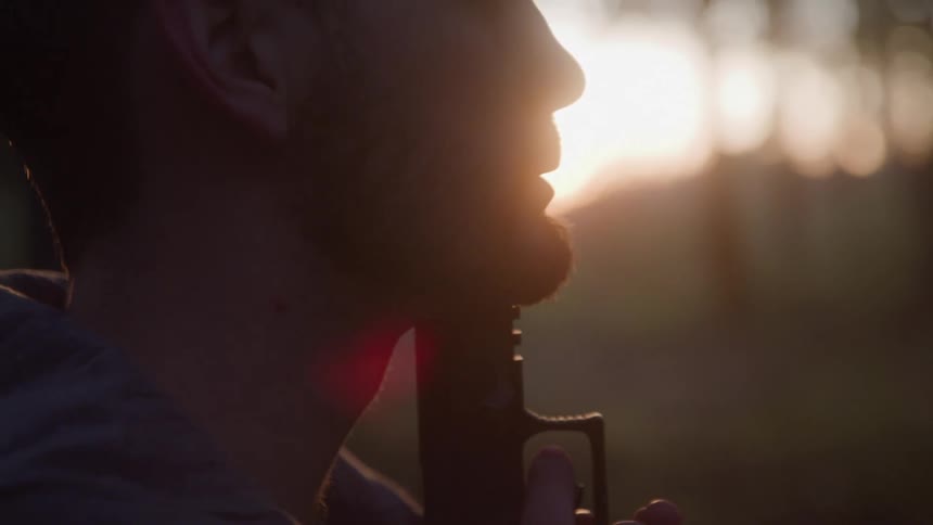 Man pointing a gun at his chin in an outdoor setting