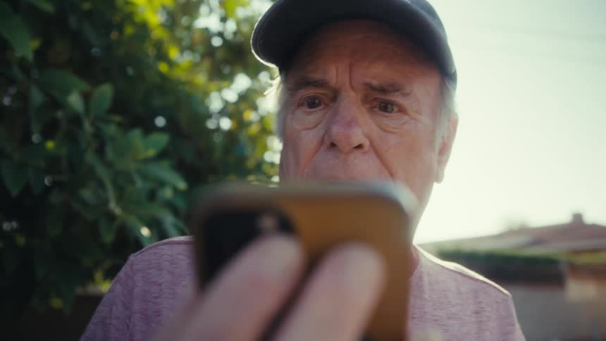Elderly man in cap looking surprised at smartphone screen