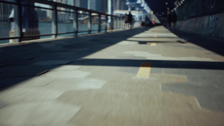 A walkway in the city with a handrail bordering the ocean at midday as people walk by