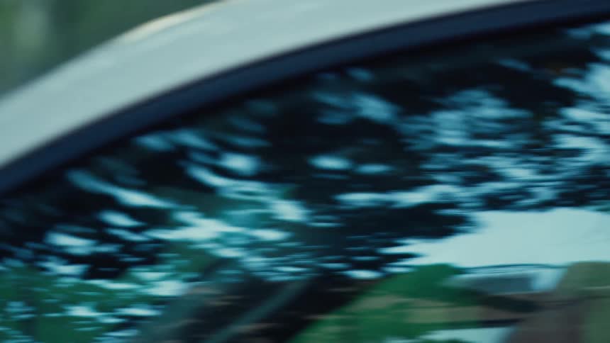 Vehicle parked near a park reflects its surroundings while people enjoy the park after dusk