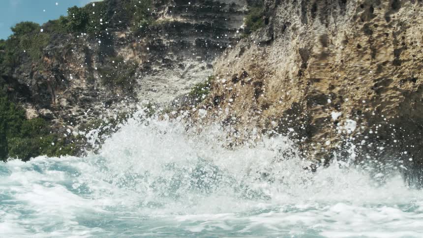 Ocean waves hit a rocky island at midday causing a series of splashes