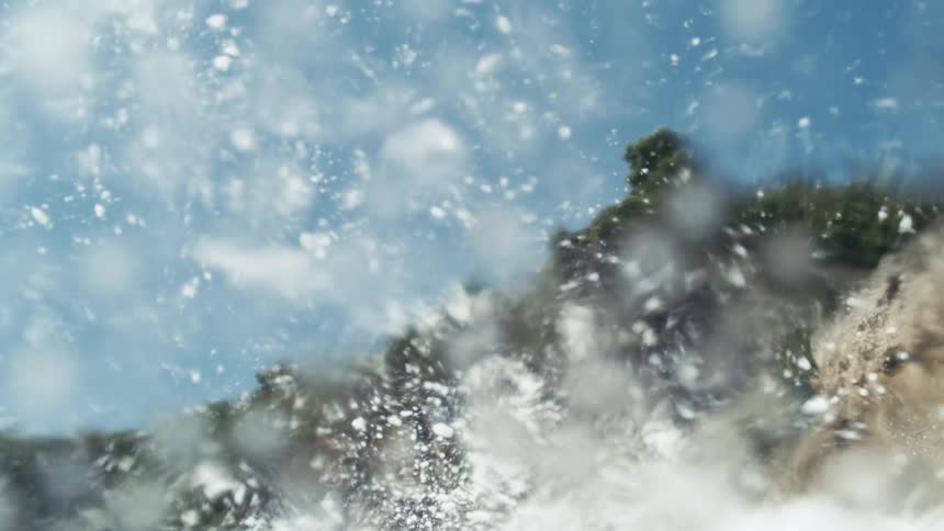 A wave crashes by the green cliff