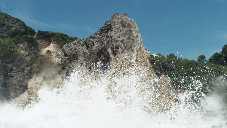 A watersplashed lens captures a blurry view of blue sky and distant cliffs