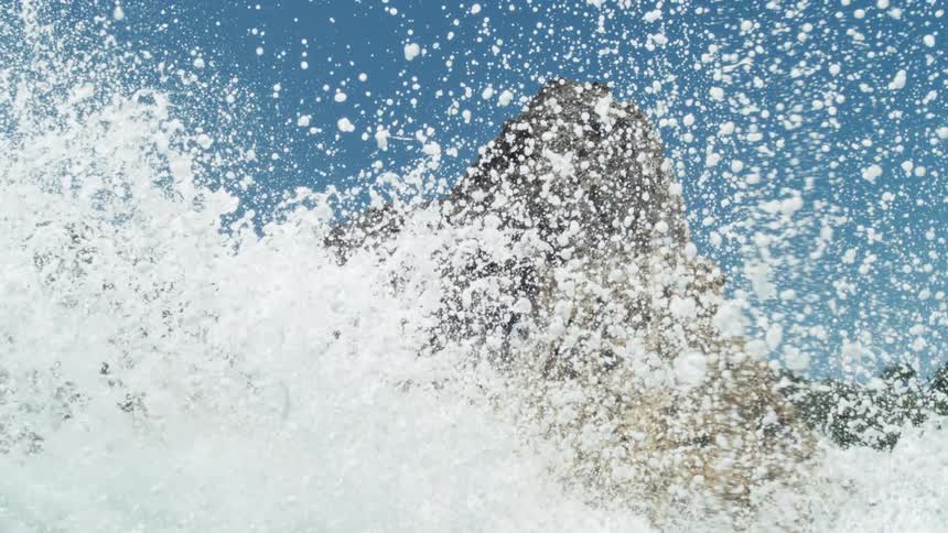 Ocean waves crash against a rocky shoreline on a sunny day