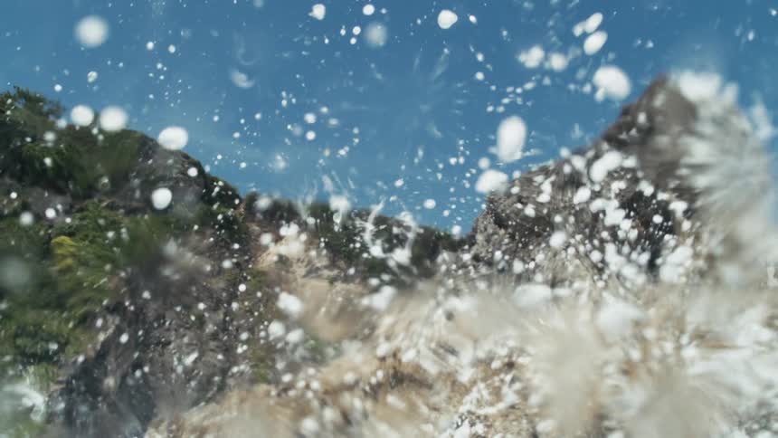 Large splashing in the ocean causes foam that partially blocks the view of the mountains