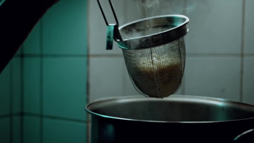 Cook shakes a long handled pasta strainer to drain freshly cooked pasta
