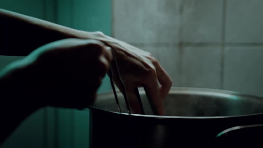 The video shows hands using tongs to strain food from a pot filled with steaming water into a metal bowl the background is a dimly lit kitchen with tiled walls