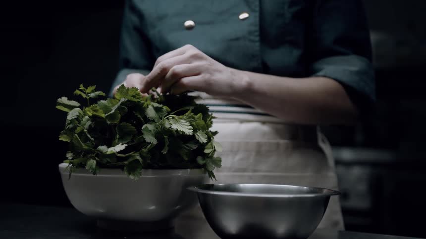 Sous chef cutting parsley leaves and placing metal cooking bowl