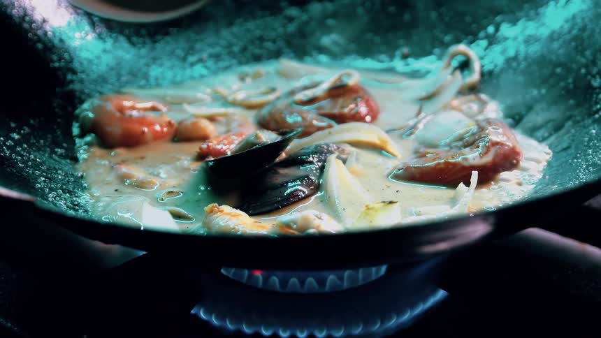 Seafood and noodles sizzle in a bubbling sauce over a blue gas flame