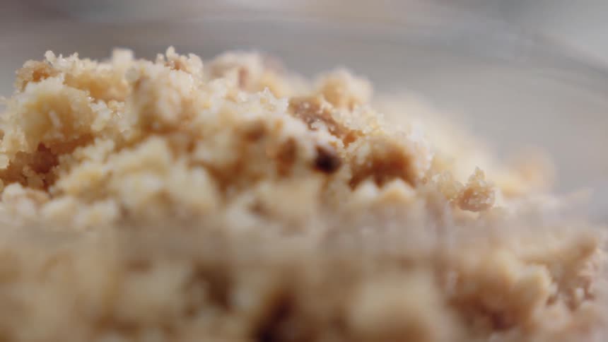 Sprinkling granular topping on top of a dry mixture in a glass bowl