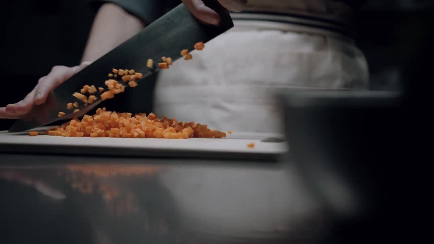 A chef cuts carrots into small pieces on a cutting board in the kitchen